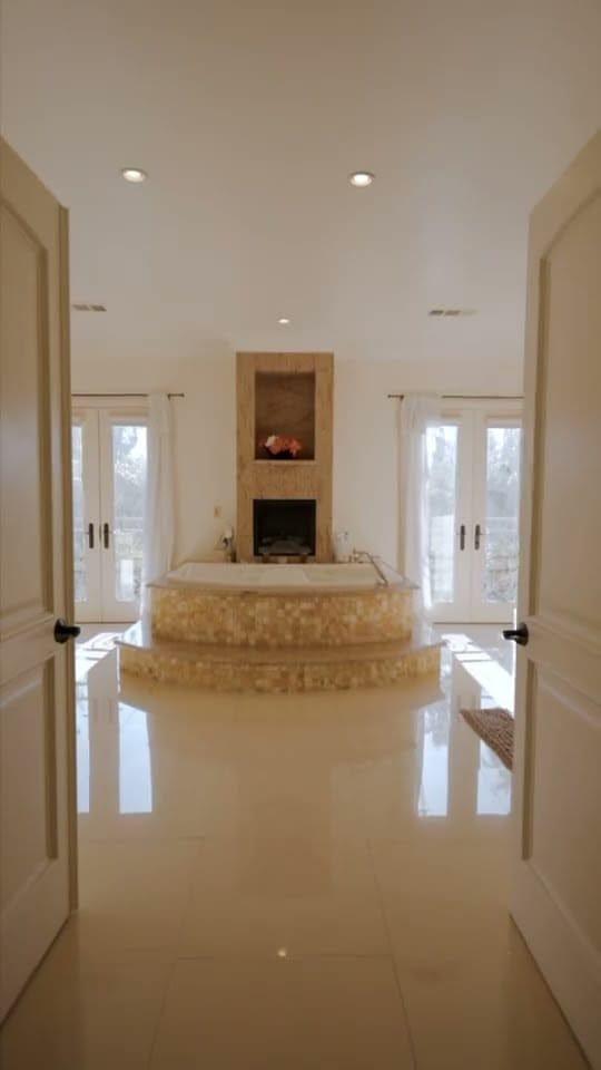 Primary bath with a raised soaking tub and fireplace between glass doors in a Tarzana home
