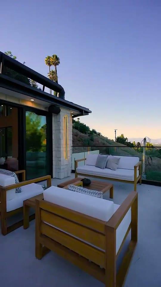Covered terrace of an Encino hillside residence at dusk, with outdoor sofas and the hillside beyond