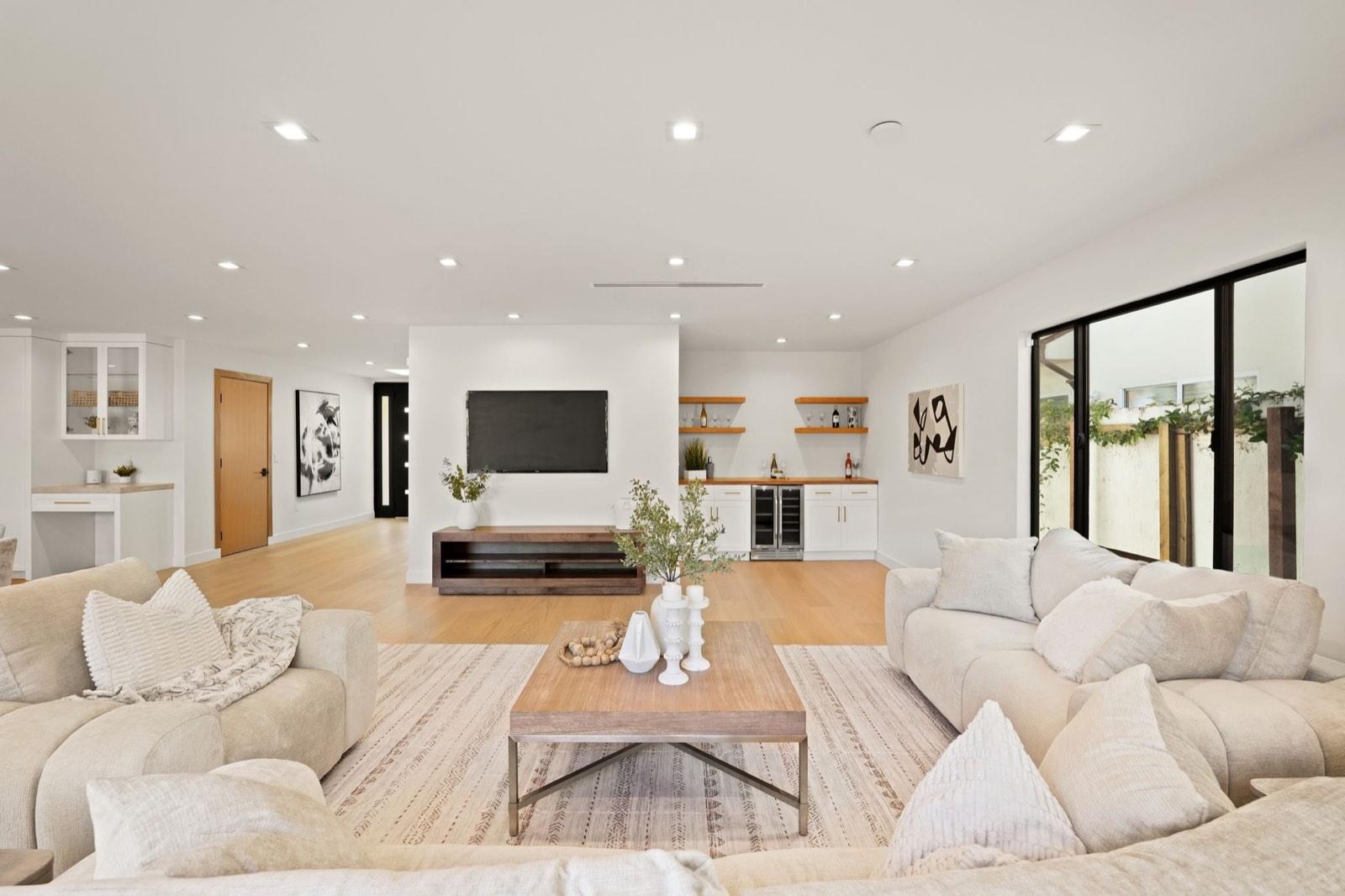 Staged living room with white sectional seating, oak flooring and recessed lighting