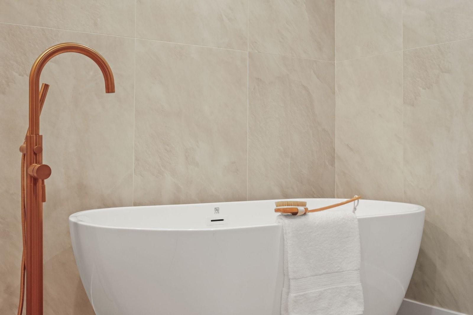 Freestanding soaking tub against a stone-tiled wall with an aged brass filler