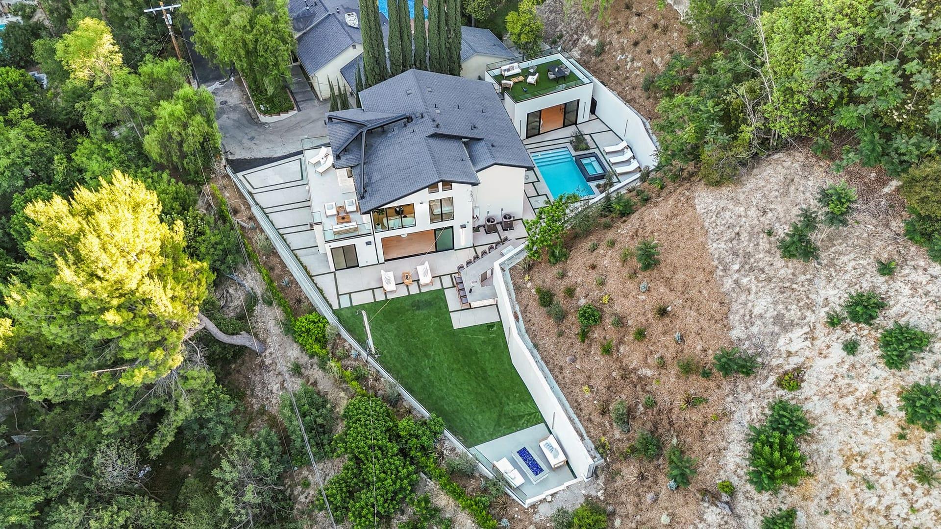 Aerial view of a hillside home in Encino on its terraced lot, with the pool, lawn and surrounding trees