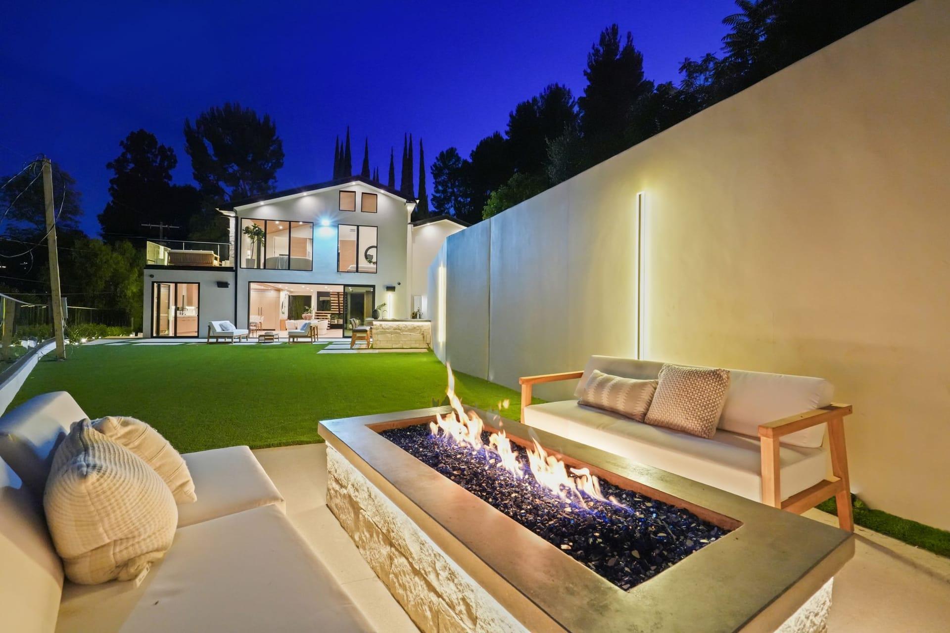 Fire table burning at night on the lawn of the the Encino hillside residence home, the lit rear of the house behind it