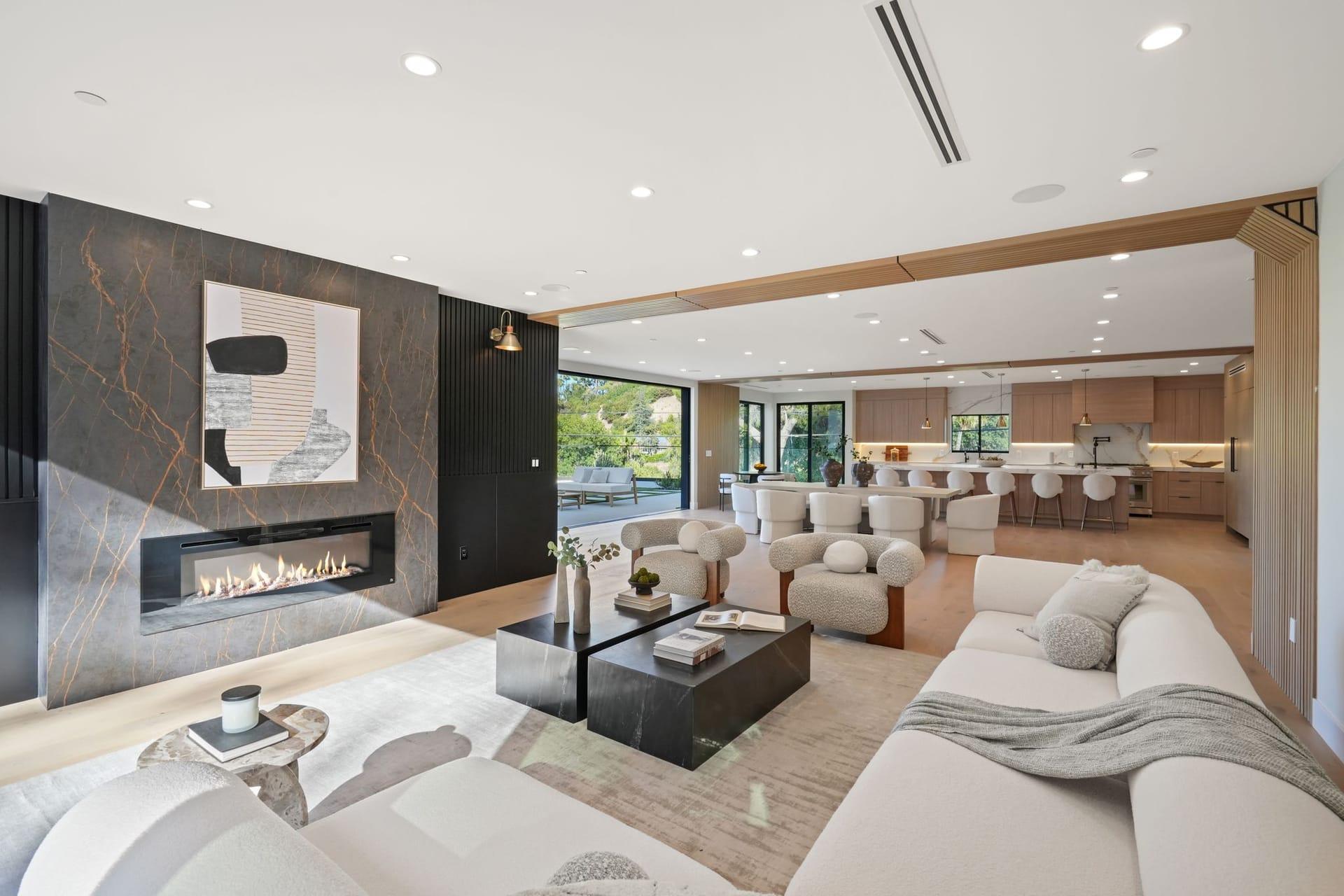 Staged living room with a linear fireplace wall, pale sofas and the dining area and kitchen beyond