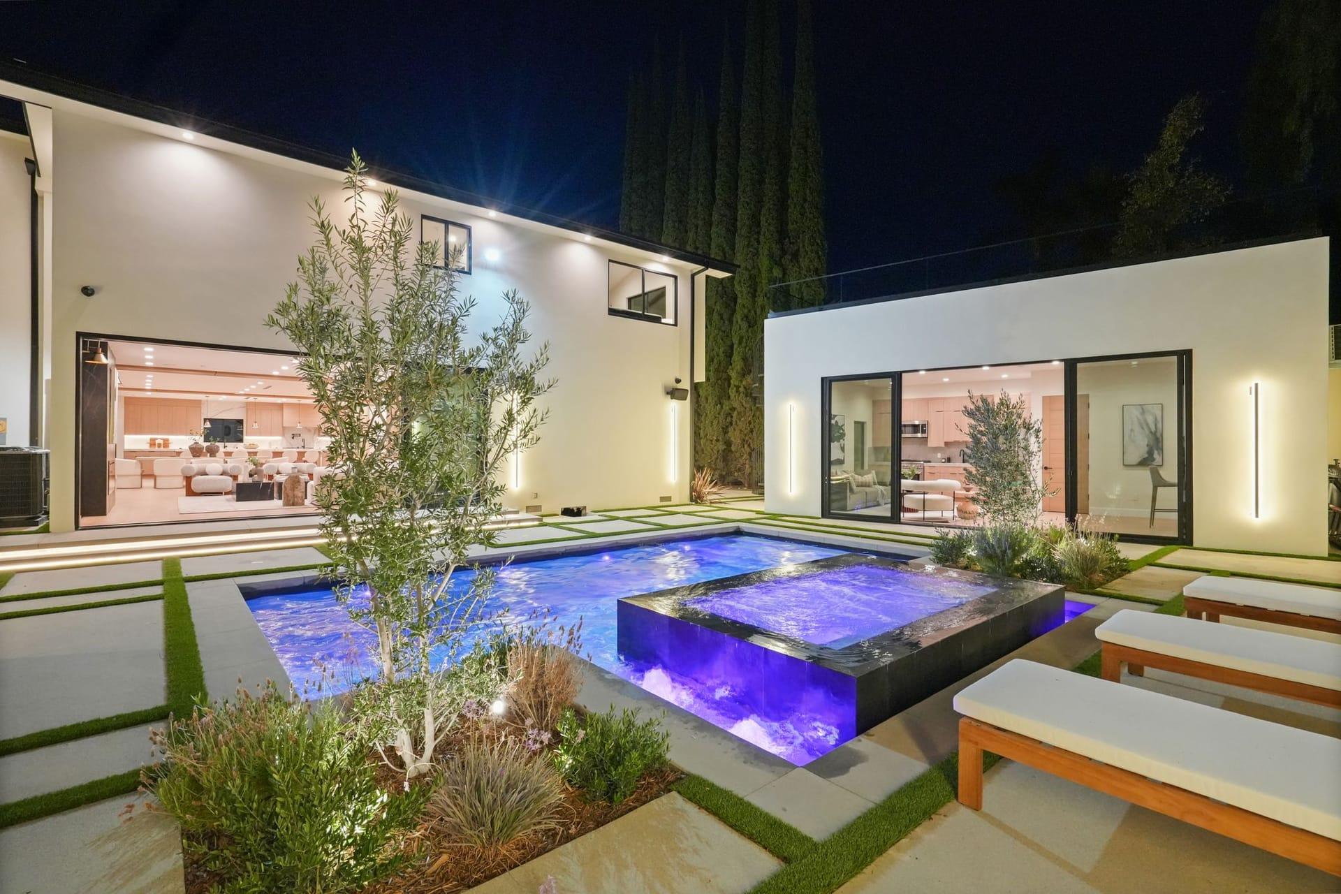 Pool and raised spa lit at night, with the glass-walled living level of the house open behind them