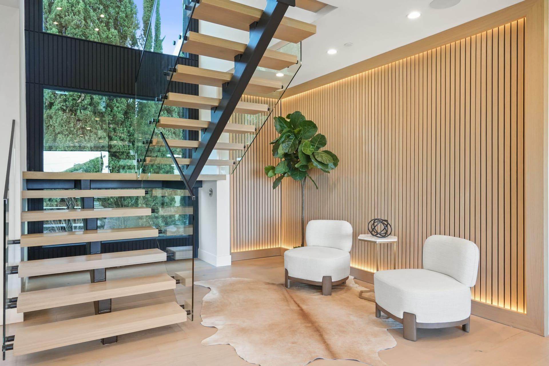 Open-tread staircase with a glass rail beside a small sitting area in a home on the Encino hillside residence, Encino