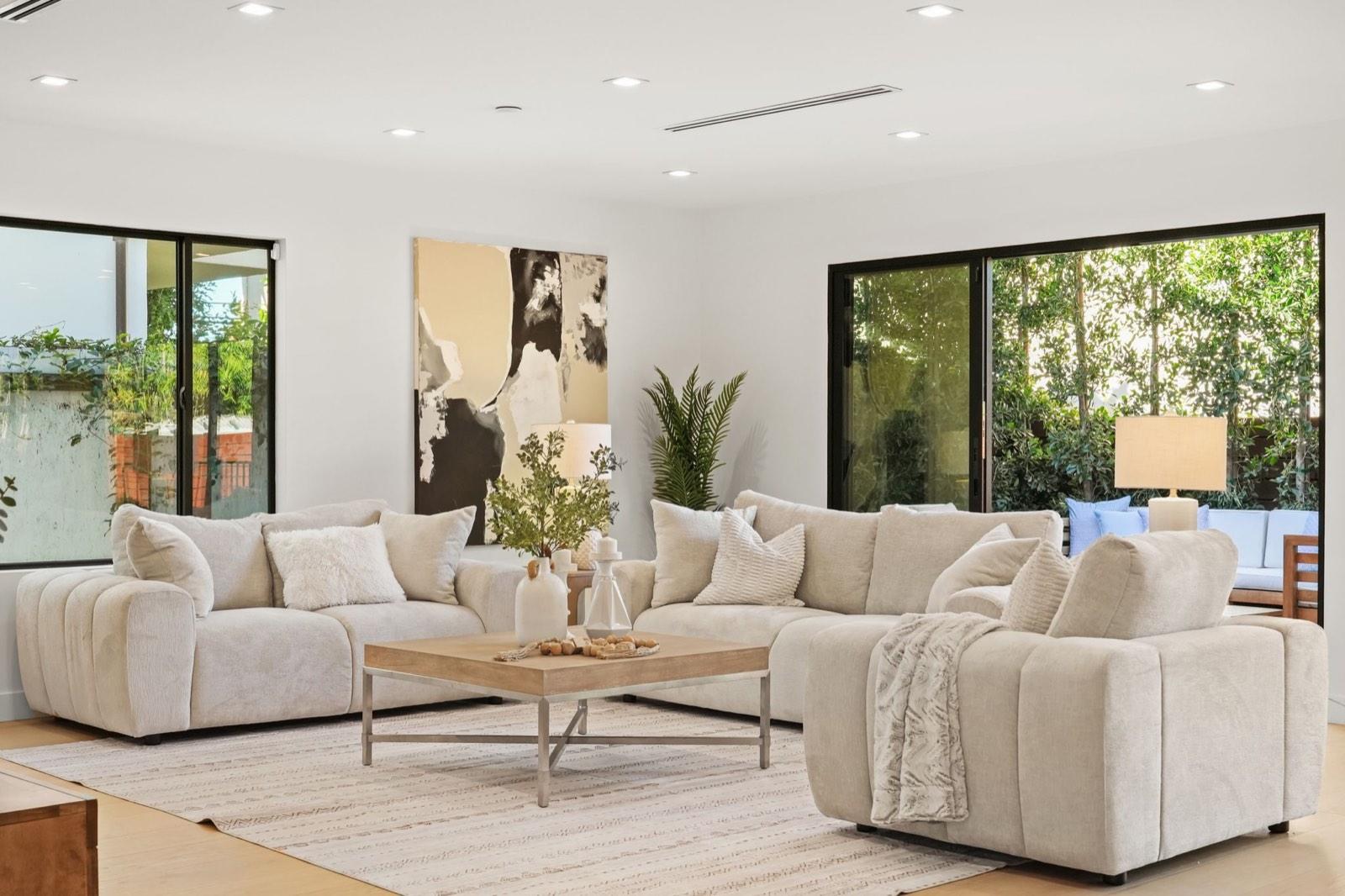 Staged living room with pale sofas, a timber coffee table and abstract artwork, black-framed glass doors to the garden behind