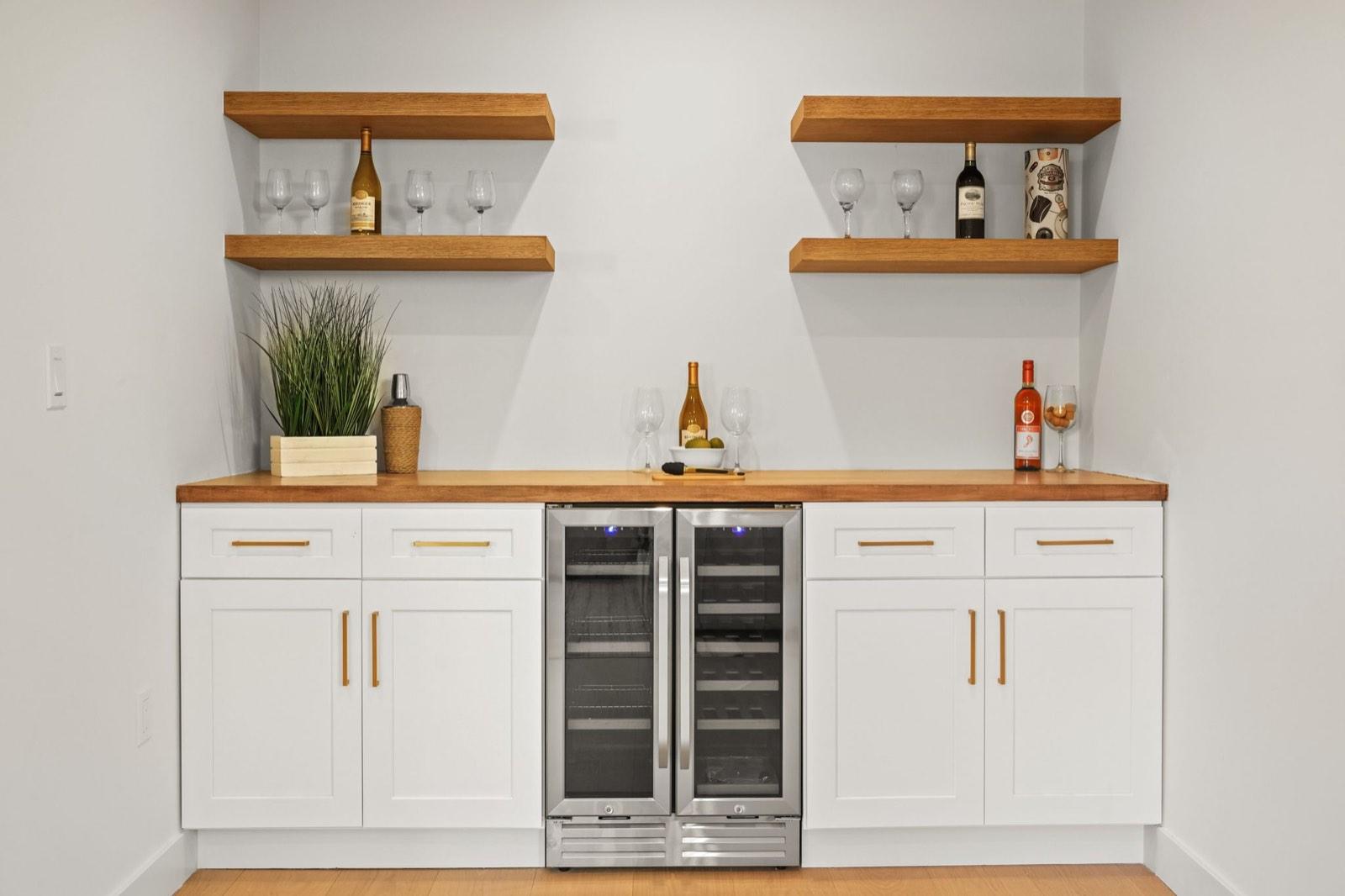 Wet bar with white cabinetry, a built-in wine refrigerator and timber open shelves styled with glassware and bottles
